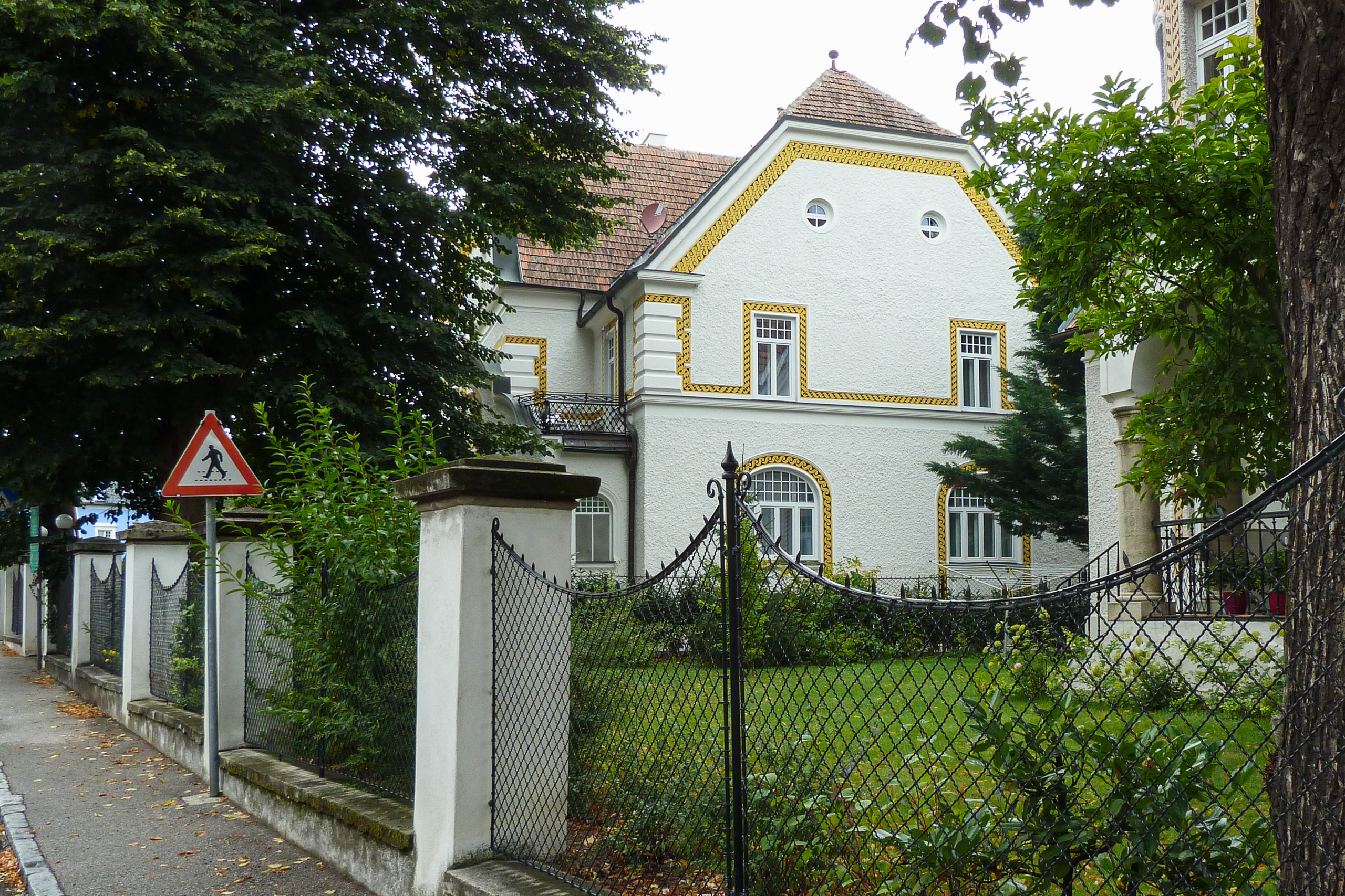 Jugendstilvilla mit goldenem Zierband hinter dem Gartenzaun